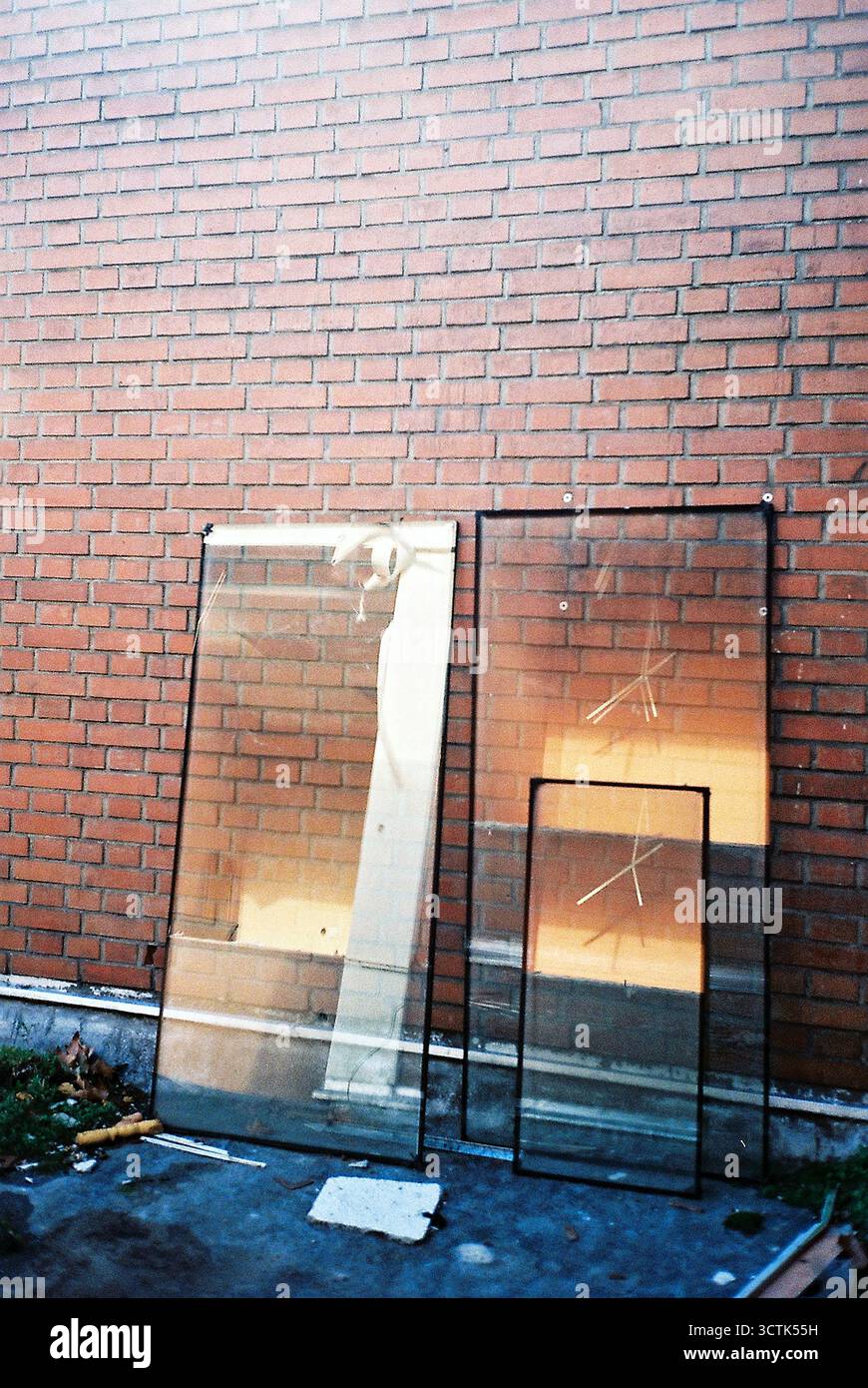Fensterscheiben, die an einer roten Ziegelwand gestapelt sind, wurden analog in einem vertikalen Rahmen aufgenommen, mit hellen Sonnenreflexionen auf dem Glas. Stockfoto