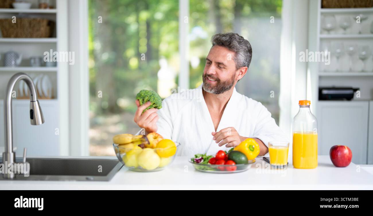 Ein reifer Mann frühstückt in der Küche mit frischem Müsli und Milch. Man isst gesundes Mittagessen genießt einen nahrhaften Salat und Gemüse zu Hause. Leckerer Snack Stockfoto
