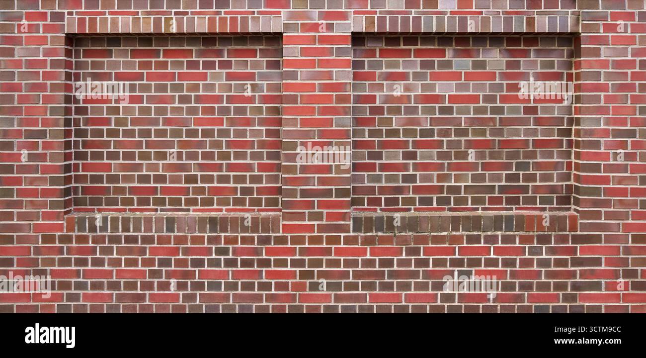Braungrau-rot gemusterte Ziegelwand mit zwei gemauerten Fensternischen Stockfoto
