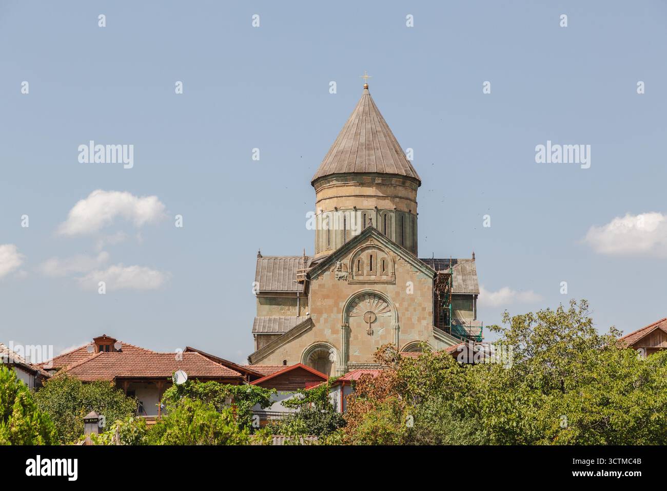 Blick auf eine alte Steinkathedrale erhebt sich über den Dächern und üppiges Grün unter einem sanften blauen Himmel in Mzcheta, Mzcheta-Mtianeti, Georgia. Stockfoto