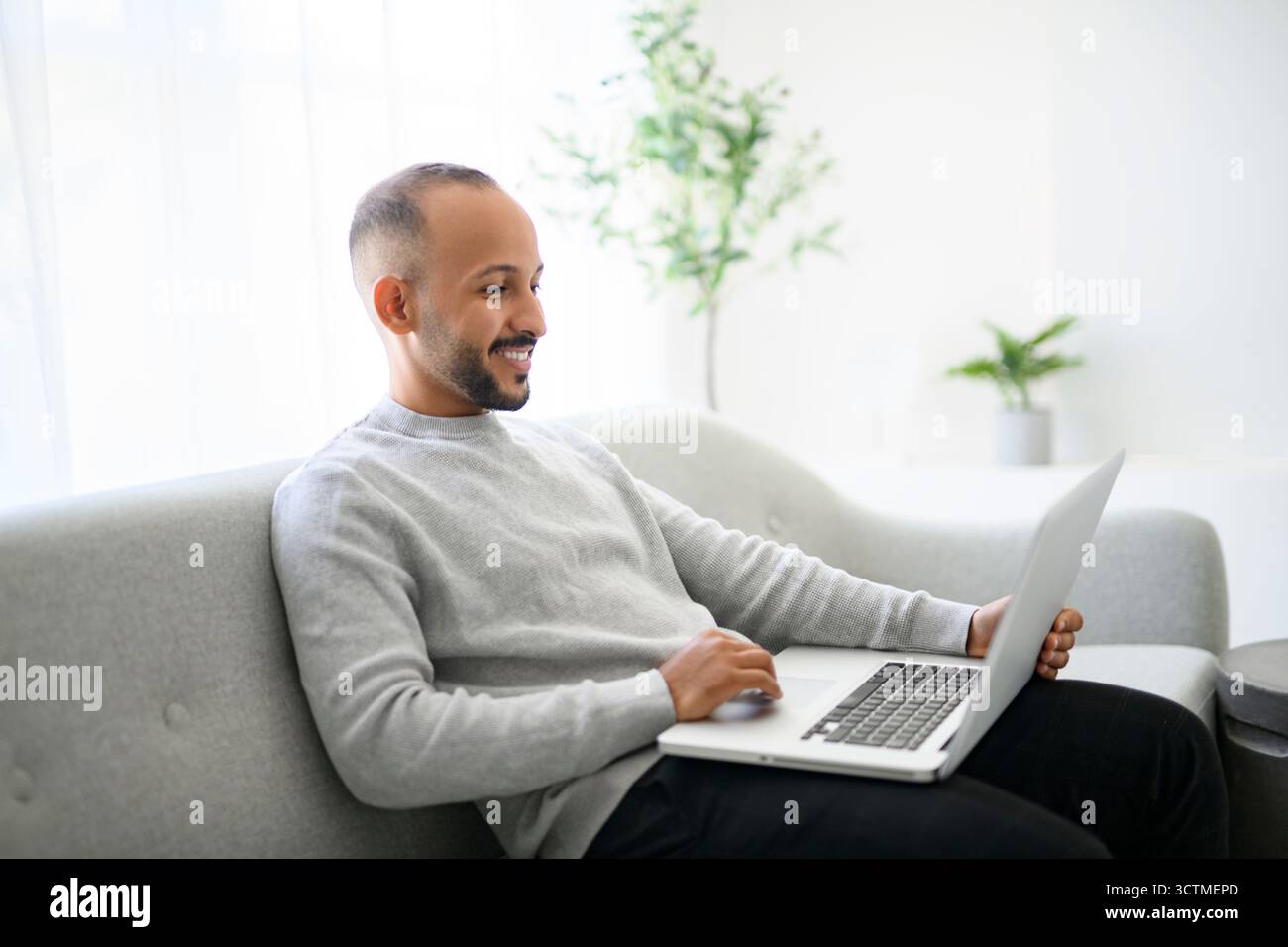 Junger islamischer arabischer Mann, der zu Hause einen Laptop auf dem Sofa benutzt Stockfoto
