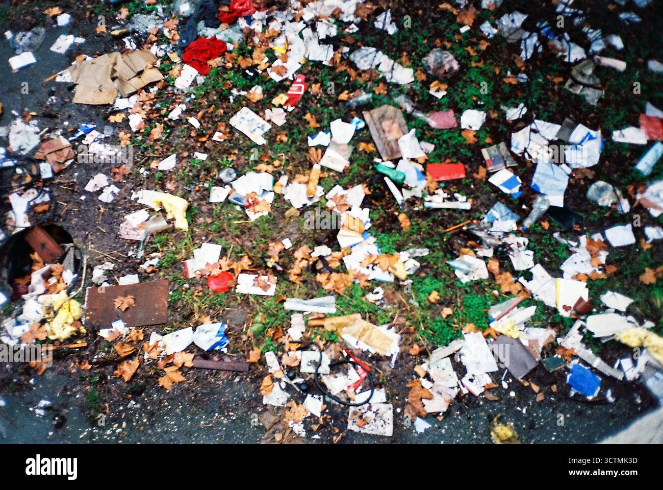 Rasen voller Müll an einem regnerischen Wintertag, aufgenommen in analogem Stil mit gedämpften Tönen und griffiger, strukturierter Filmatmosphäre. Stockfoto