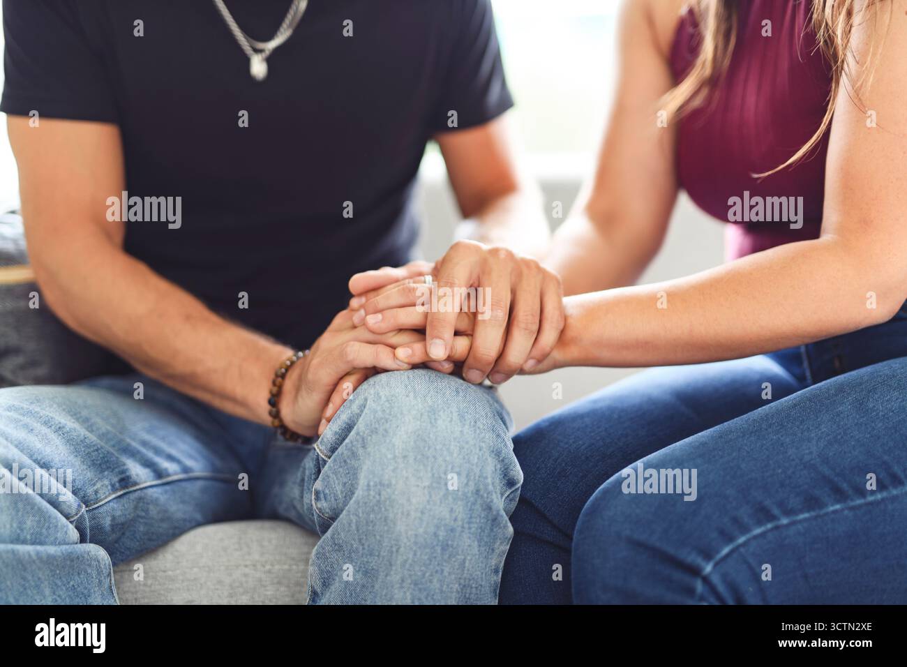 Hand in Hand durch alles. Aufnahme eines unverkennbaren Paares, das die Hände hält, während es zu Hause auf einem Sofa sitzt. Stockfoto