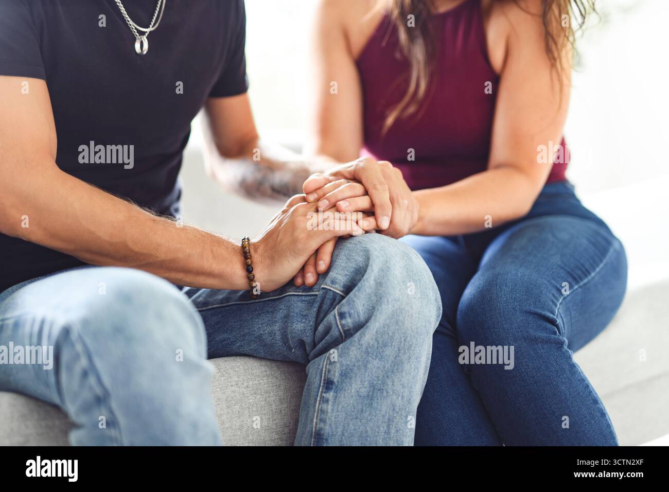 Hand in Hand durch alles. Aufnahme eines unverkennbaren Paares, das die Hände hält, während es zu Hause auf einem Sofa sitzt. Stockfoto