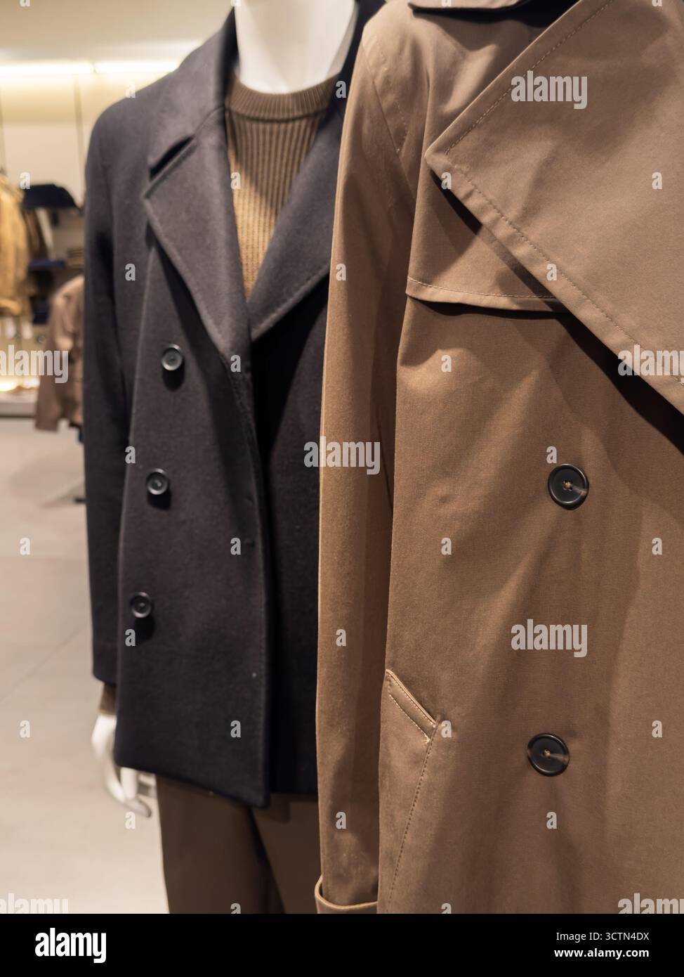 Nahaufnahme von stylischen Herbst- und Wintermänteln mit Trenchcoat und Erbsenmänteln in saisonalen Farben. Zeigt klassische und moderne Oberbekleidung-Trends im Modehandel. Stockfoto