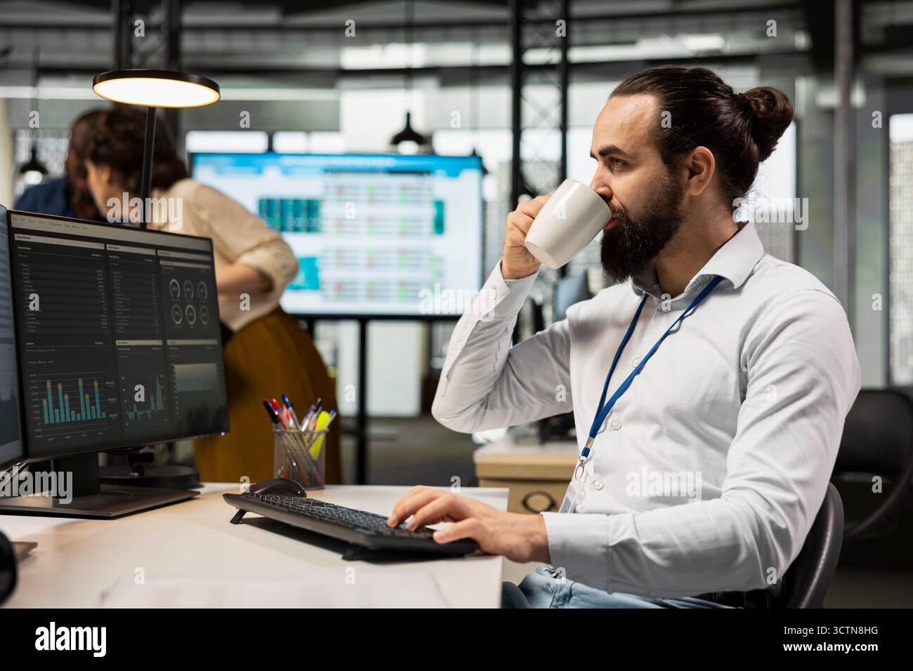 Der Mitarbeiter trinkt Kaffee, während er Analysen und KPI-Kennzahlen auf Monitor überprüft, die Geschäftsstrategie vorantreibt und eine professionelle Einstellung aufrechtzuerhalten, die auf Ziele und Erfolg ausgerichtet ist. Stockfoto