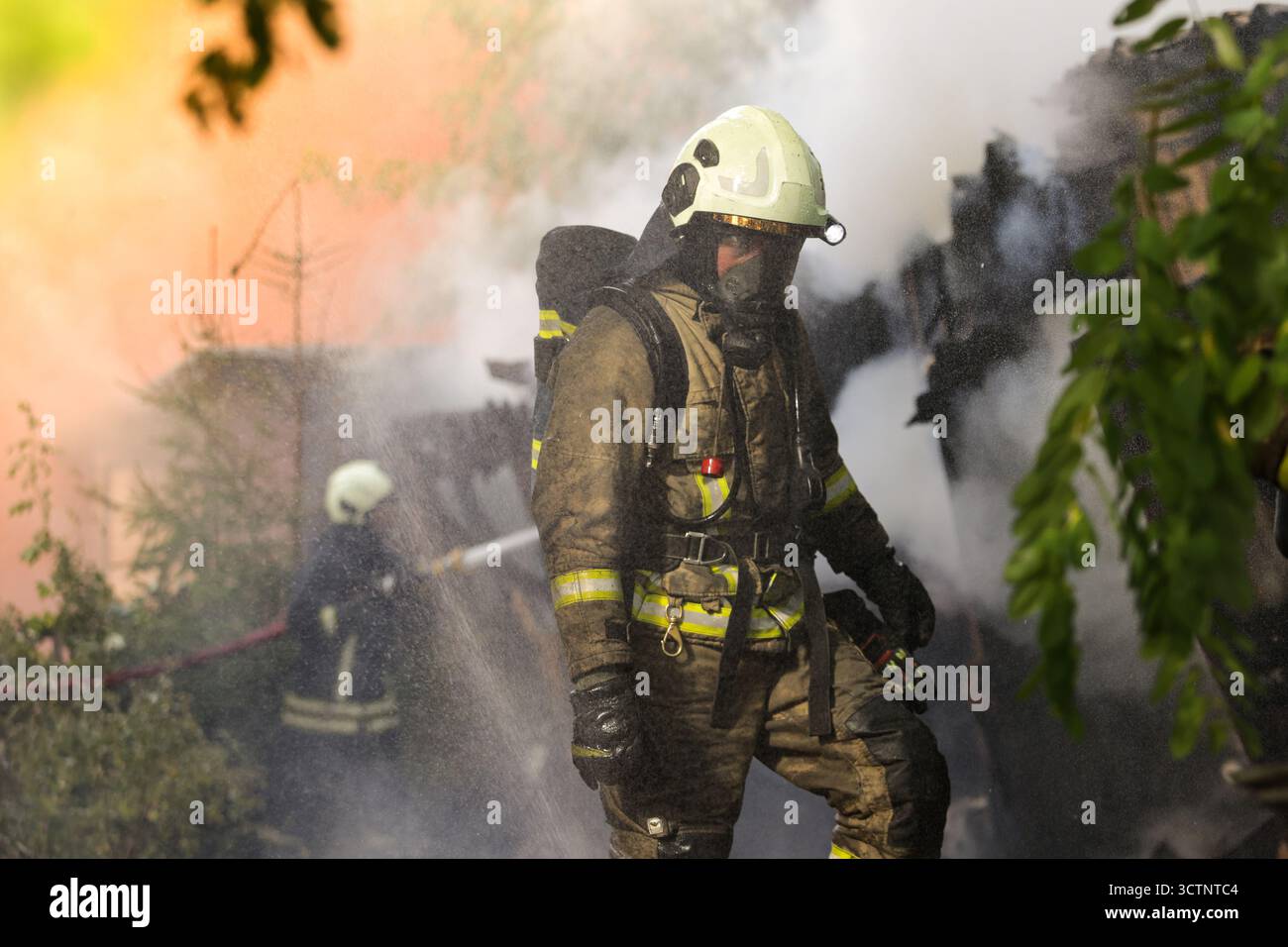 Ein professioneller Feuerwehrmann in Helm und Schutzanzug, der in dichtem Rauch am Brandort steht Stockfoto