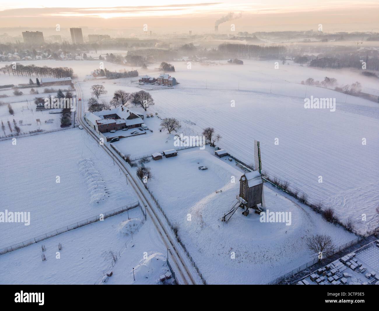 Luftaufnahme einer weißen Winterlandschaft mit der Windmühle Luizenmolen im Vordergrund und der Stadt Anderlecht und der Skyline von Brüssel Stockfoto