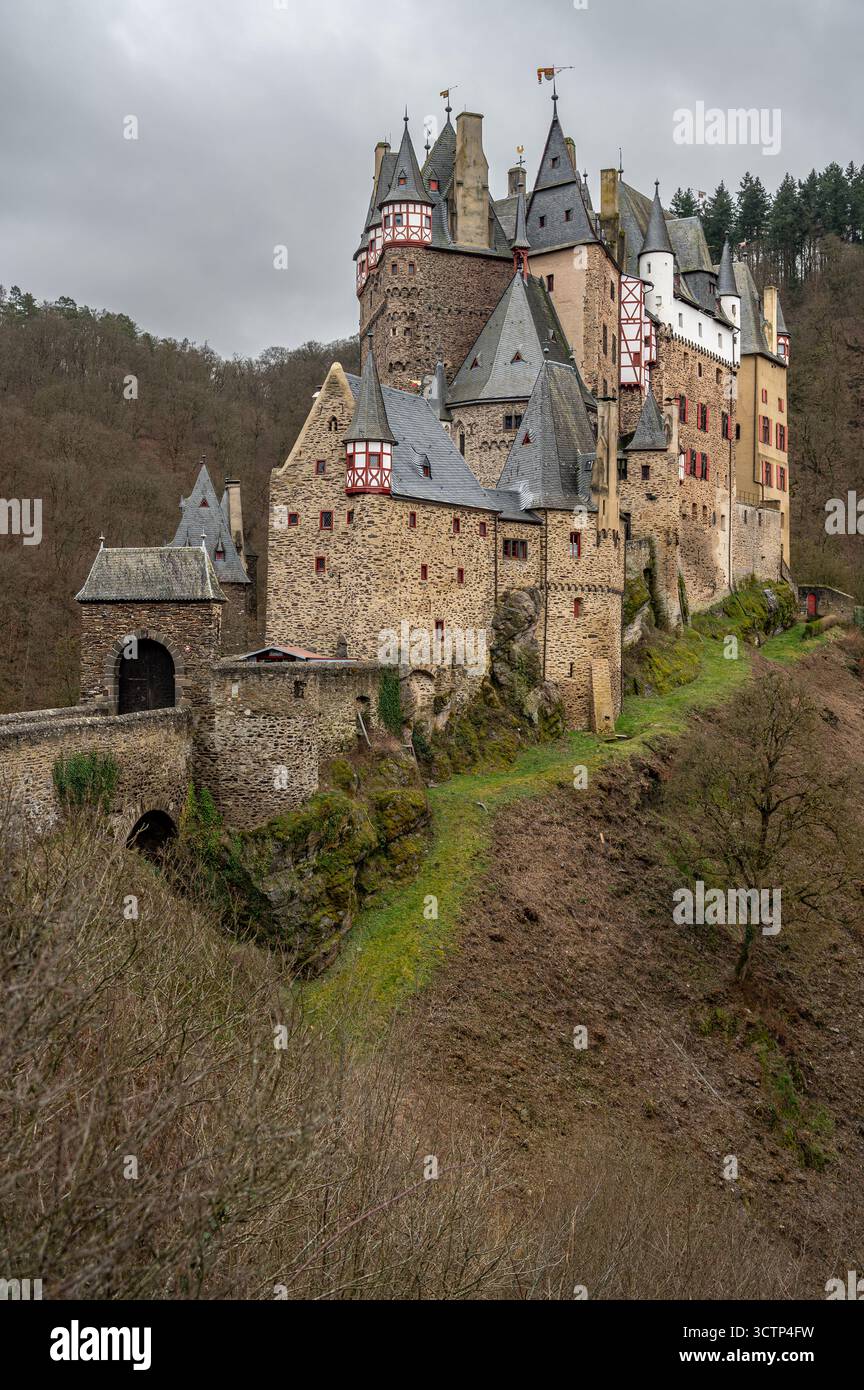 Schräger Blick auf die Burg Eltz, umgeben von blattlosen Bäumen an einem bewölkten Tag, mit Blick auf die mittelalterlichen Türme und die bewaldete Umgebung. Stockfoto