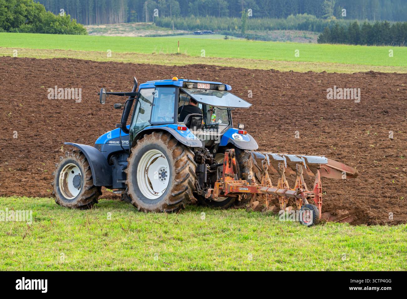 Traktor mit Pflug, landwirtschaftliche Pflugmaschine, die im Herbst/Herbst auf einem Feld in den belgischen Ardennen, Luxemburg, Wallonien, Belgien arbeitet Stockfoto