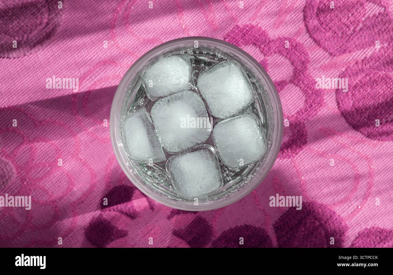 Ein Blick von oben auf ein erfrischendes Getränk mit Eis. Oberseite der Becheroberfläche mit Eiswürfeln und einem klaren Getränk auf rosafarbenem Hintergrund. Einzigartige Vorschläge Stockfoto