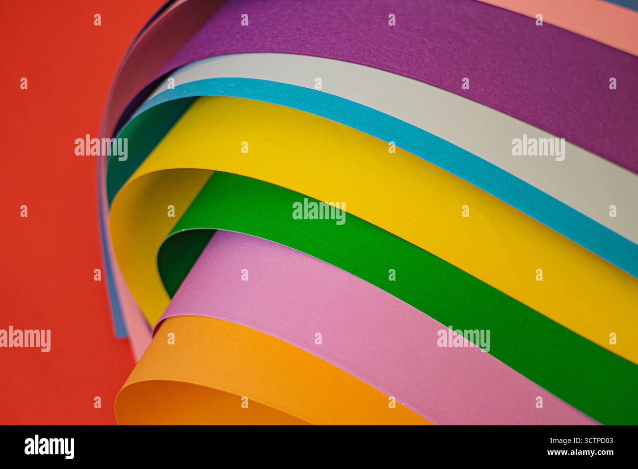 Bunte Papierbögen in einem geschwungenen, mehrschichtigen Muster vor einem leuchtend roten Hintergrund. Bietet ein breites Spektrum an Farbtönen. Selektiver Fokus. Stockfoto