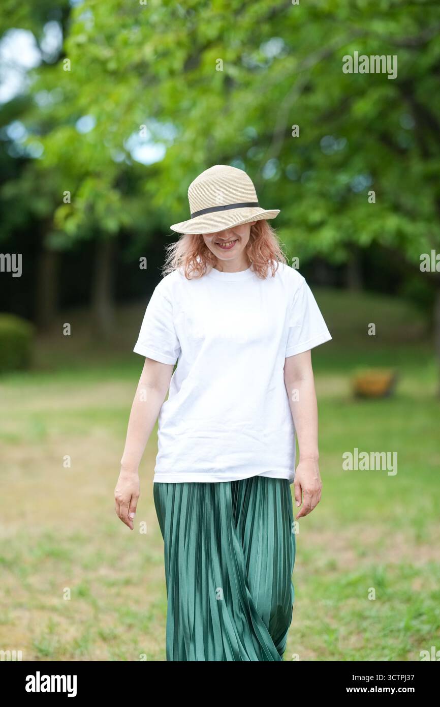 Eine Frau mit Strohhut und grünem Rock spaziert in einem Park. Sie lächelt und genießt ihre Zeit im Freien Stockfoto