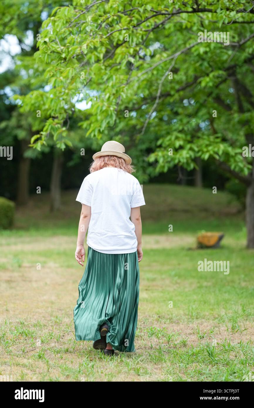Eine Frau mit Strohhut und grünem Rock geht durch ein grasbewachsenes Feld. Die Szene ist friedlich und ruhig, die Frau blickt in die Ferne Stockfoto