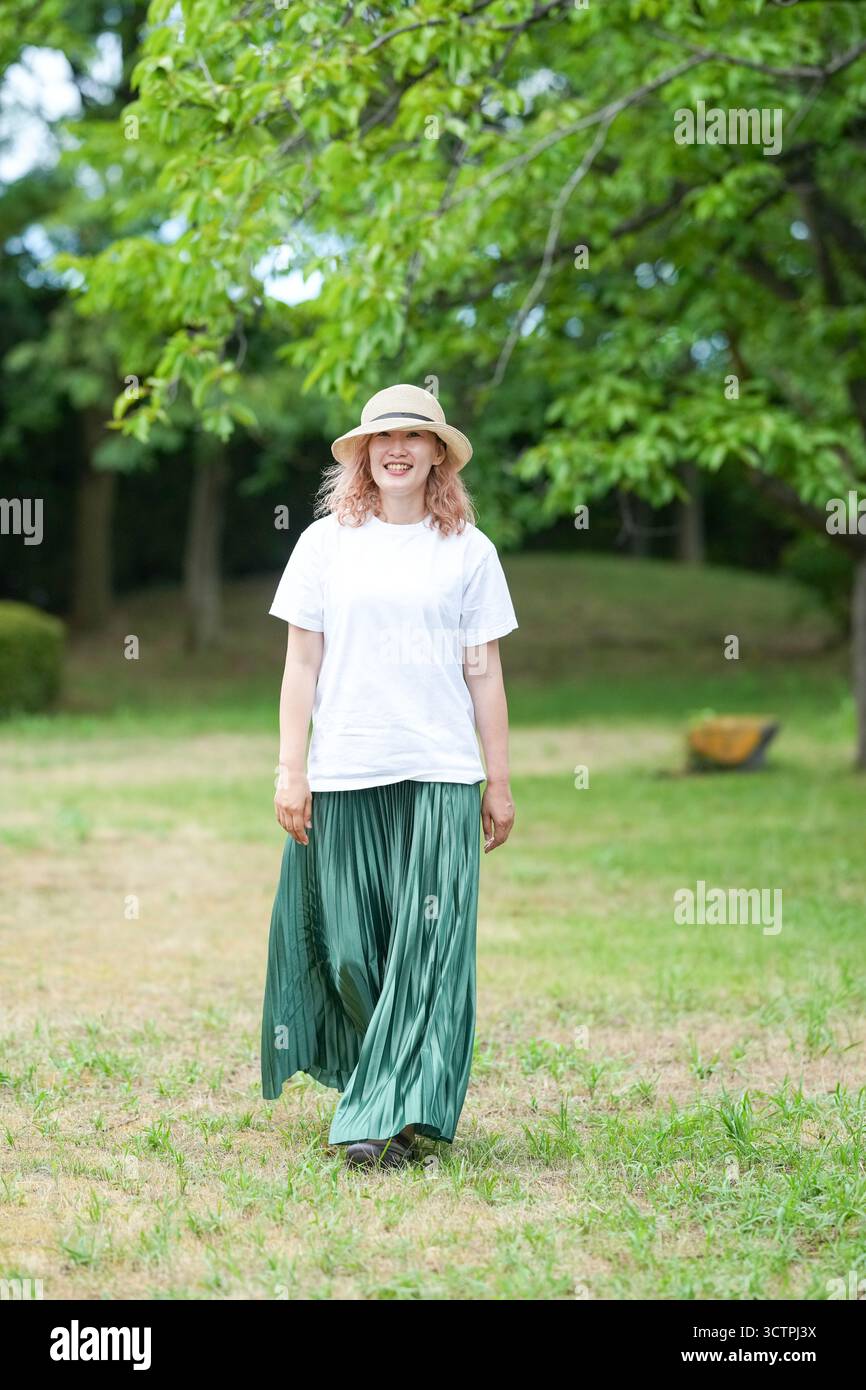 Eine Frau mit Strohhut und grünem Rock läuft in einem Park. Sie lächelt und genießt ihre Zeit im Freien Stockfoto