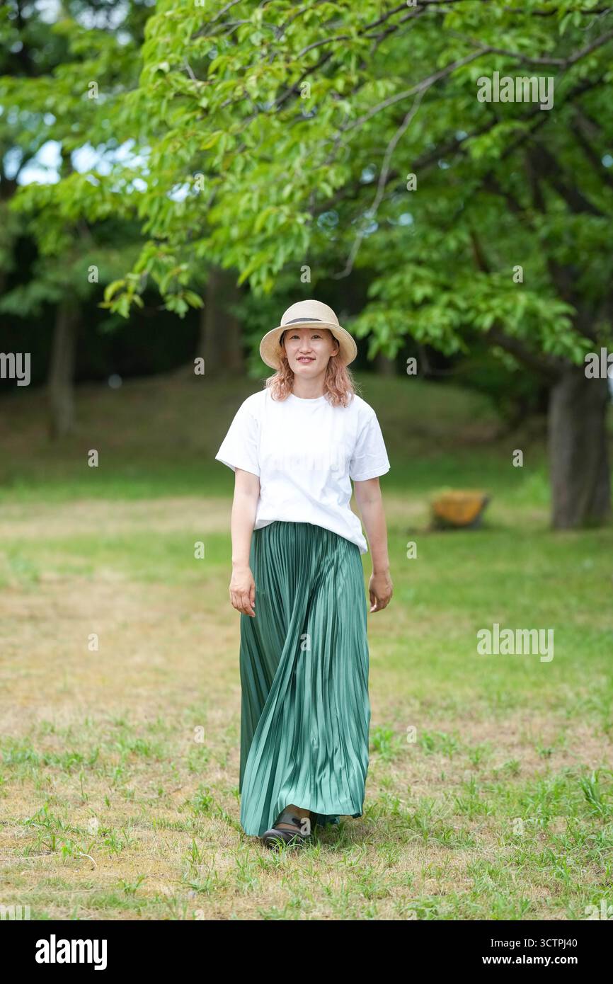 Eine Frau mit grünem Rock und Strohhut läuft in einem Park. Die Szene ist friedlich und ruhig, die Frau genießt die Natur Stockfoto