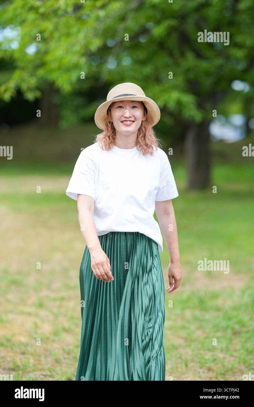 Eine Frau mit grünem Rock und Strohhut läuft in einem Park. Sie lächelt und genießt ihre Zeit im Freien Stockfoto