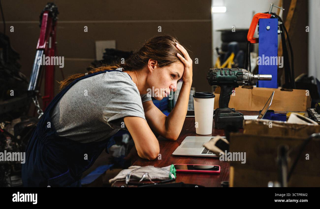 Besorgte Unternehmerin in in der Autowerkstatt mit geschäftlichen Schwierigkeiten Stockfoto