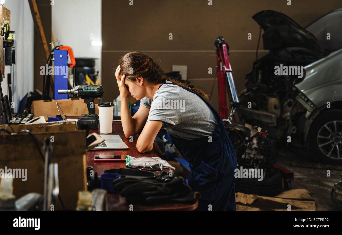 Besorgte Unternehmerin in in der Autowerkstatt mit geschäftlichen Schwierigkeiten. Konkurs eines kleinen Unternehmens. Stockfoto