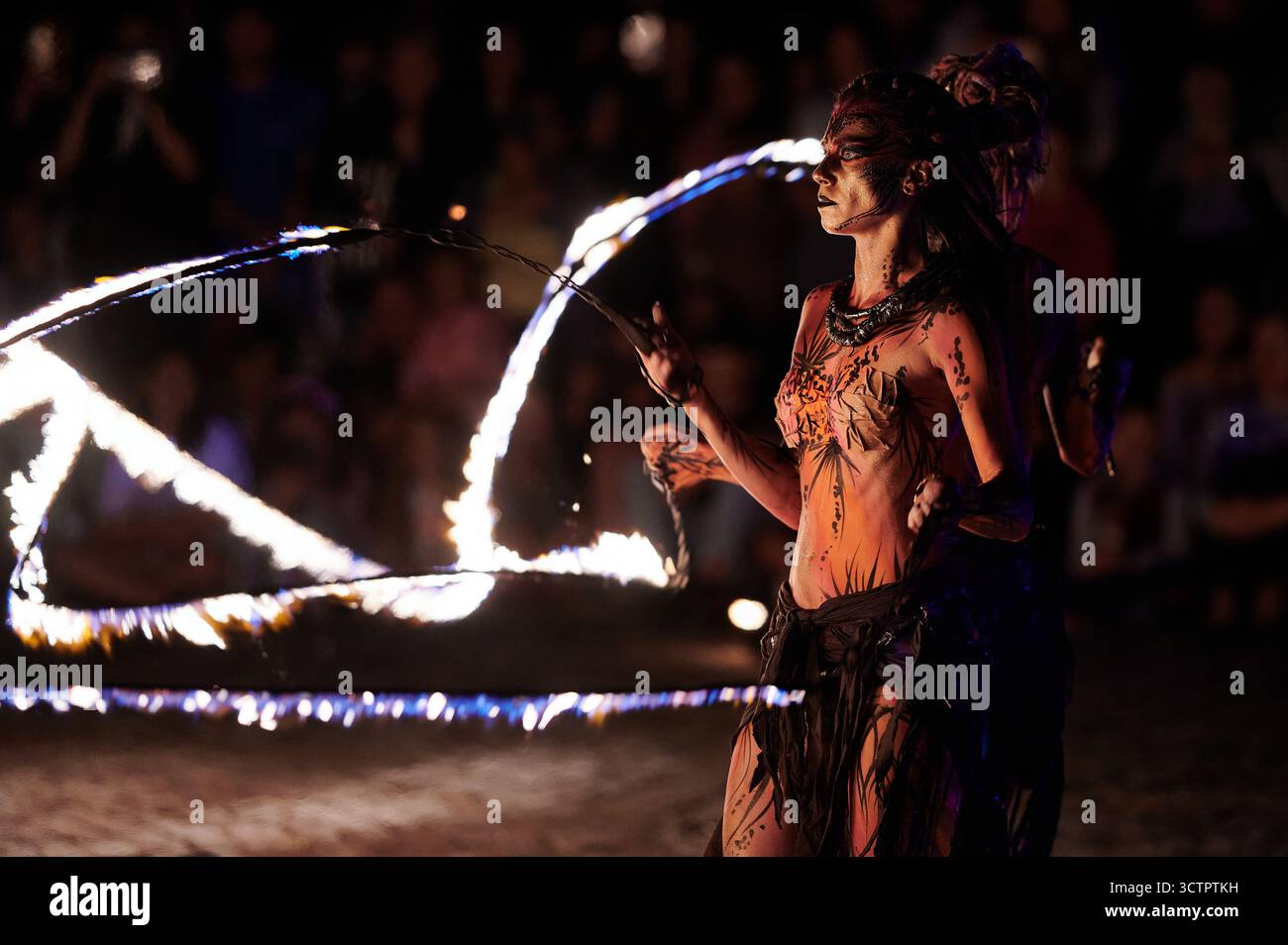 Feuertänzerin führt im Los Fuegos Fire Theatre in Polen eine sich drehende Bewegung durch und erzeugt Flammenspuren, horizontale Nachtaufnahmen mit leuchtendem Orange Stockfoto
