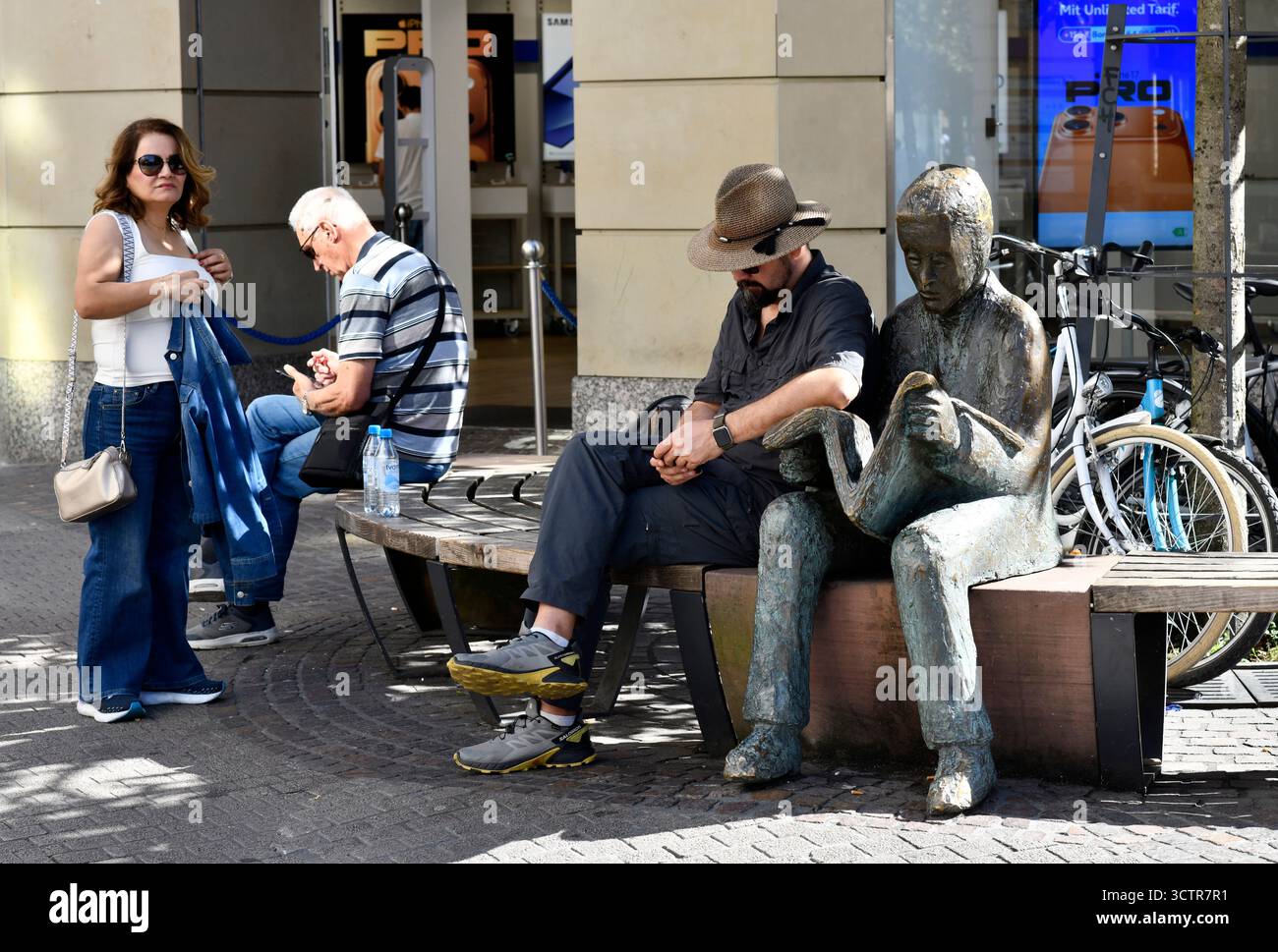Mann liest sein Smartphone, während er neben einer Statue eines Mannes sitzt, der eine Zeitung in Heidelberg im Südwesten Deutschlands liest. Stockfoto