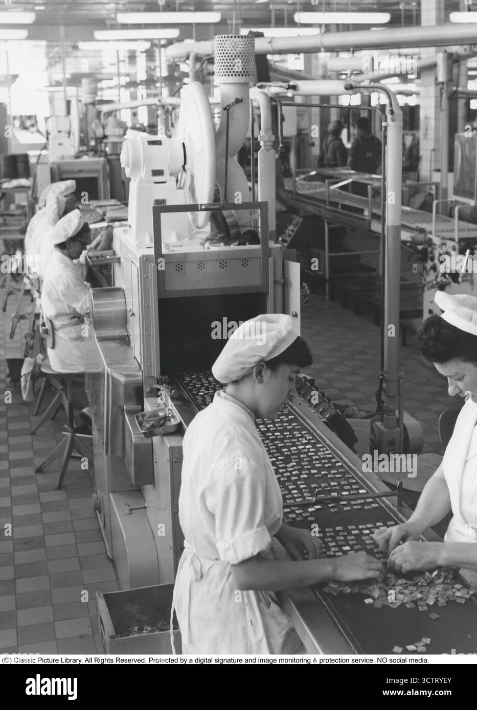 Ab Marabou, Sundbyberg 1957. Frauen sitzen an einem Förderband, während Marabous Marzipanpralinen ihre glänzende Schokoladenbeschichtung in der so genannten Enrobing-Maschine erhalten. Rund eine halbe Million Pralinen passieren in jeder Schicht entlang der Linie. Marabou wurde 1916 gegründet und entwickelte sich schnell zu einem der beliebtesten Schokoladenproduzenten Schwedens. Das Werk in Sundbyberg, kurz vor den Toren Stockholms, war jahrzehntelang der Hauptproduktionsstandort. In den 1950er Jahren setzte sich Marabou für die Herstellung von Süßwaren im industriellen Maßstab ein, wobei Präzisionsmaschinen mit handwerklicher Arbeit kombiniert wurden, die oft von Frauen ausgeführt wurde. Stockfoto