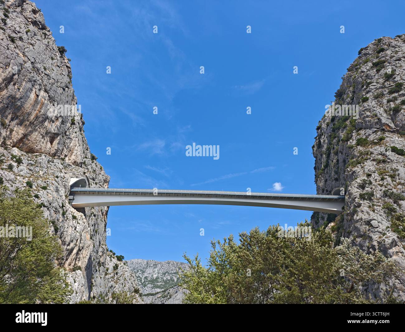 Eine moderne Brücke erstreckt sich zwischen zwei hohen Felsformationen und zeigt beeindruckende Ingenieurskunst inmitten einer malerischen Landschaft. Der helle Himmel verstärkt das B Stockfoto