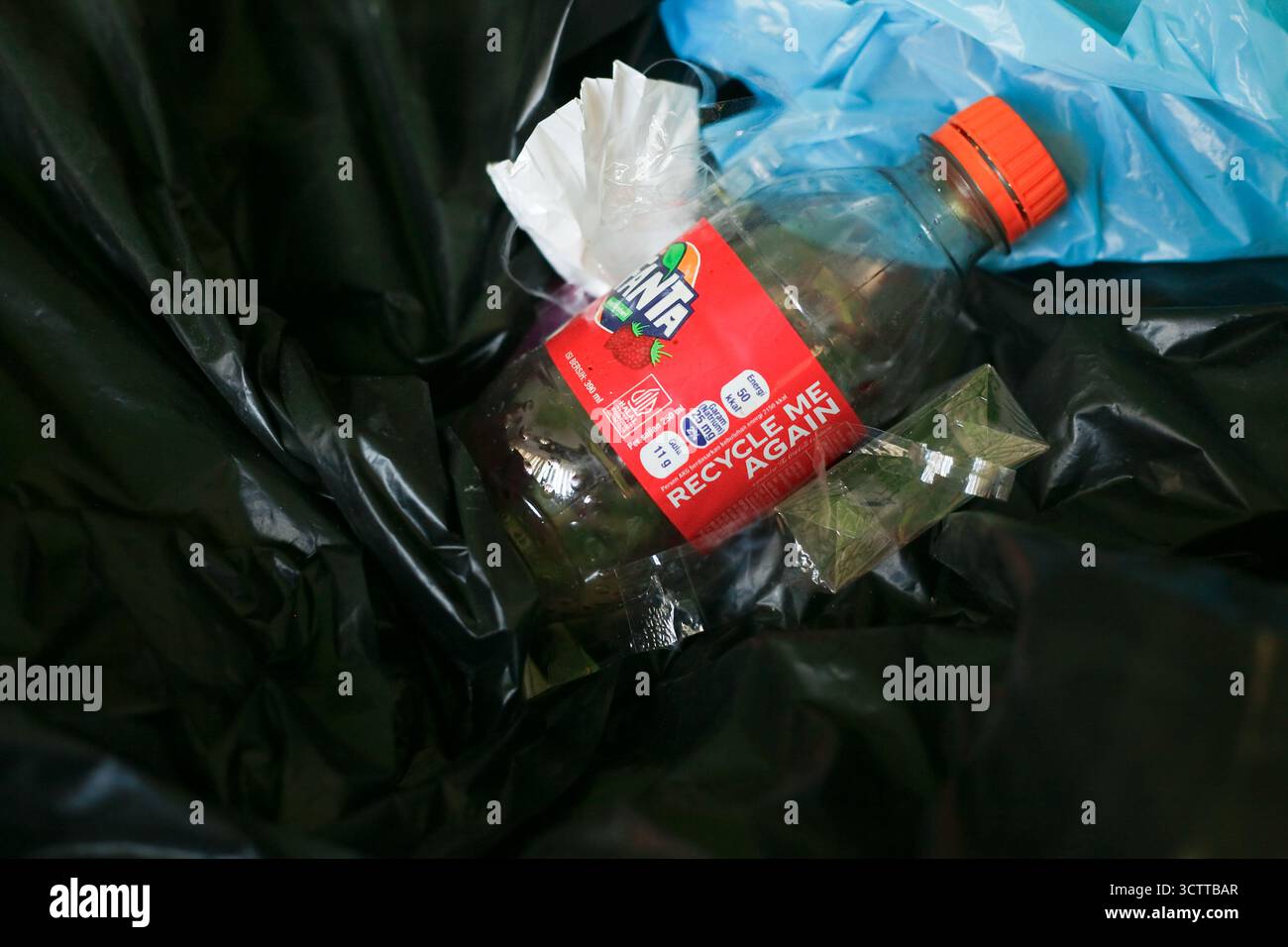 Schließen Sie eine Plastikflasche Fanta mit Textwort, recyceln Sie mich wieder auf Müllbeutel Stockfoto