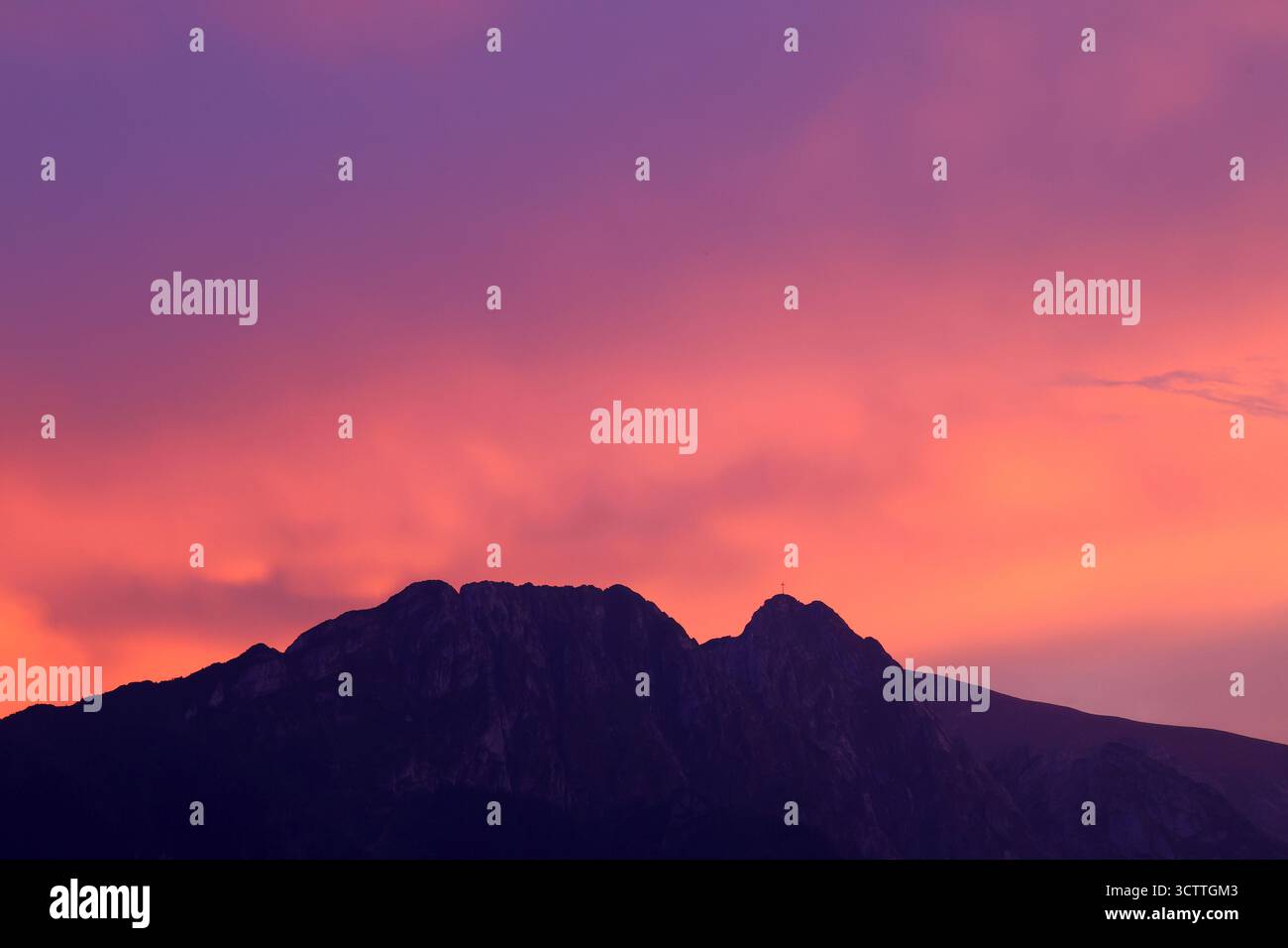 Dramatische Silhouette des Giwont-Berges mit einem Kreuz auf der Spitze vor einem lebendigen Sonnenunterganghimmel, Tatra, Polen Stockfoto