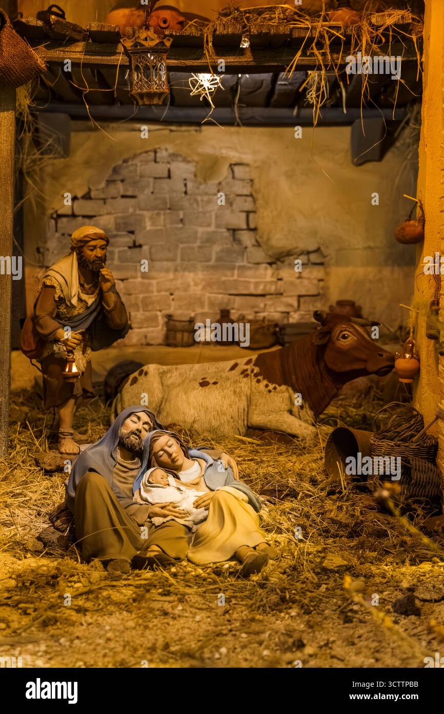 Heilige Familie schläft in einem rustikalen Stall mit einer Kuh und einer Laterne in der Nähe. Stockfoto