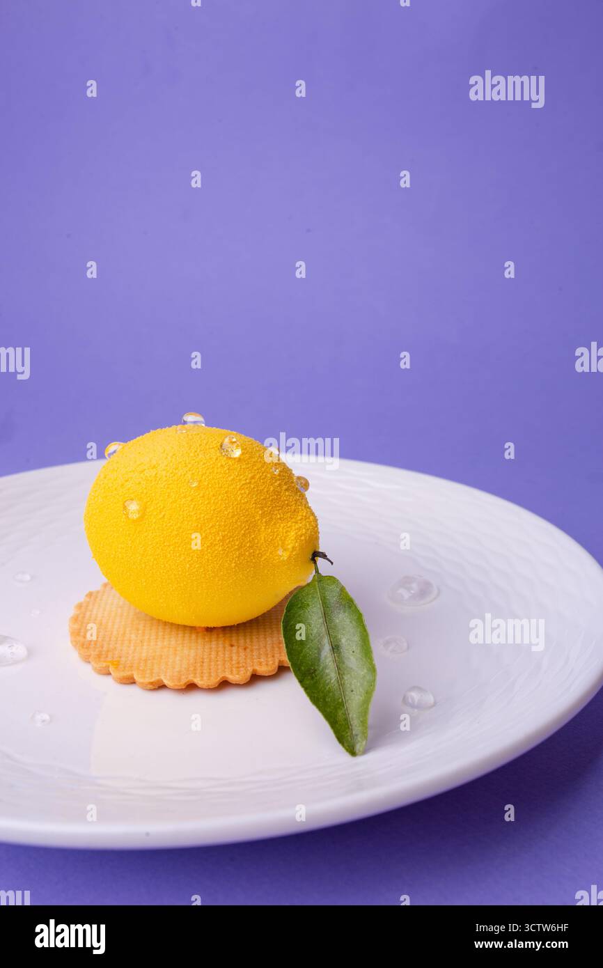 Ein hyperrealistisches, zitronenförmiges Dessert mit Wassertröpfchen und einem einzelnen Blatt, serviert auf einem strukturierten weißen Teller. Perfekt für Konditoreien, Sommermänner Stockfoto