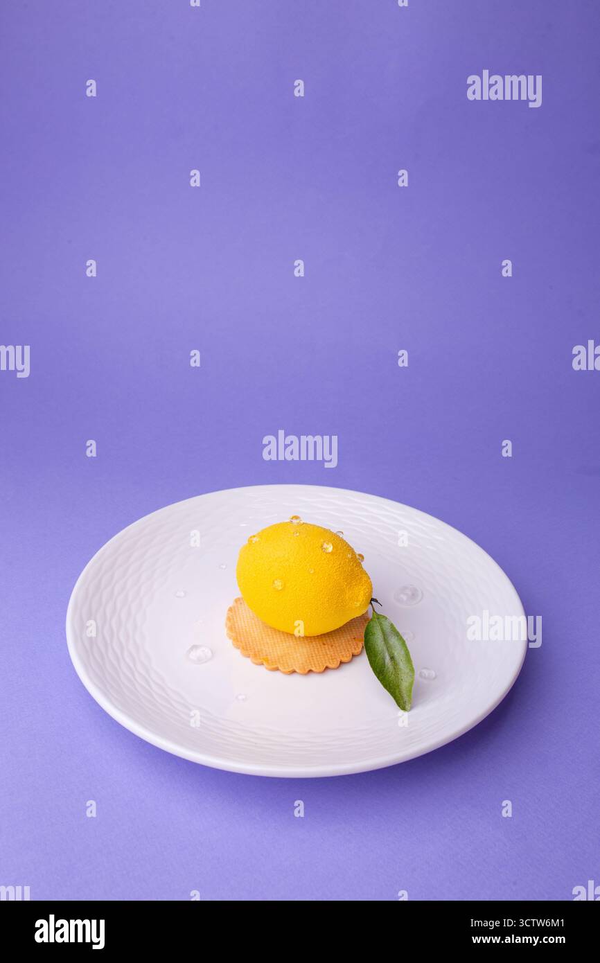 Ein hyperrealistisches, zitronenförmiges Dessert mit Wassertröpfchen und einem einzelnen Blatt, serviert auf einem strukturierten weißen Teller. Perfekt für Konditoreien, Sommermänner Stockfoto