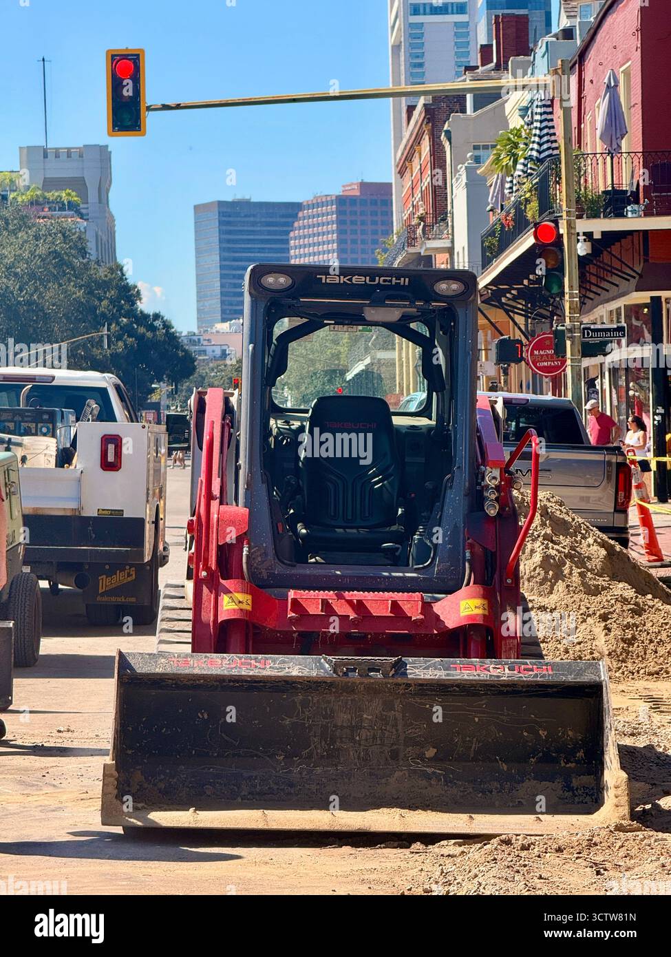 Kleiner Baubagger, der auf einer schmalen Stadtstraße in New Orleans, Louisiana, USA, geparkt ist, mit bunten Gebäuden und Bäumen, die die Straße unter A säumen Stockfoto