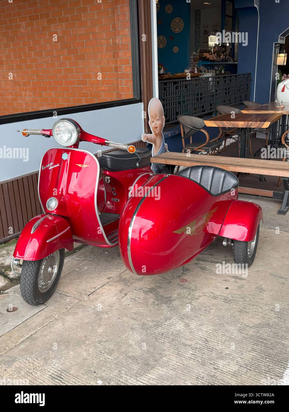 Bangkok, Thailand - 27. September 2025: Ein wunderschön restaurierter roter Vespa-Roller mit passendem Beiwagen, der vor einem Café parkt. Stockfoto
