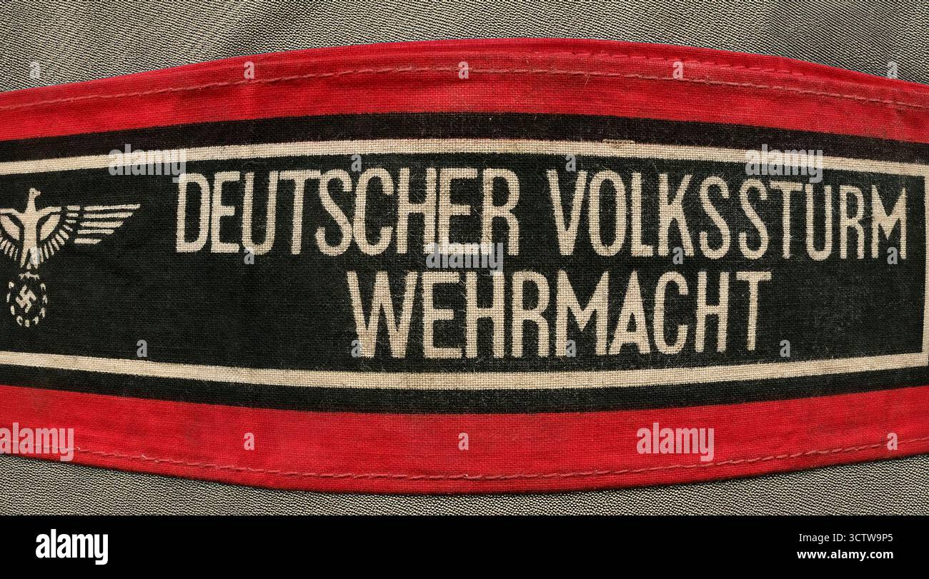 Wehrmachtsarmband des Deutschen Volkssturms, das während des Zweiten Weltkriegs von Mitgliedern des Volkssturms getragen wurde. Der Volkssturm war eine deutsche Nationalmiliz, die in den letzten Kriegsmonaten gegründet wurde. Sie bestand aus Männern zwischen 13 und 60 Jahren, die nicht bereits im Militärdienst waren. Das Armband ist mit einem schwarzen Band in der Mitte mit weißem Text versehen und der Nationaladler hält auf beiden Seiten ein Hakenkreuz. Das Stoffarmband eines letzten Keuschs führte die Volksarmee dazu, den sowjetischen Vormarsch nach Nazi-Deutschland und Berlin zu behindern. WW2 Stockfoto