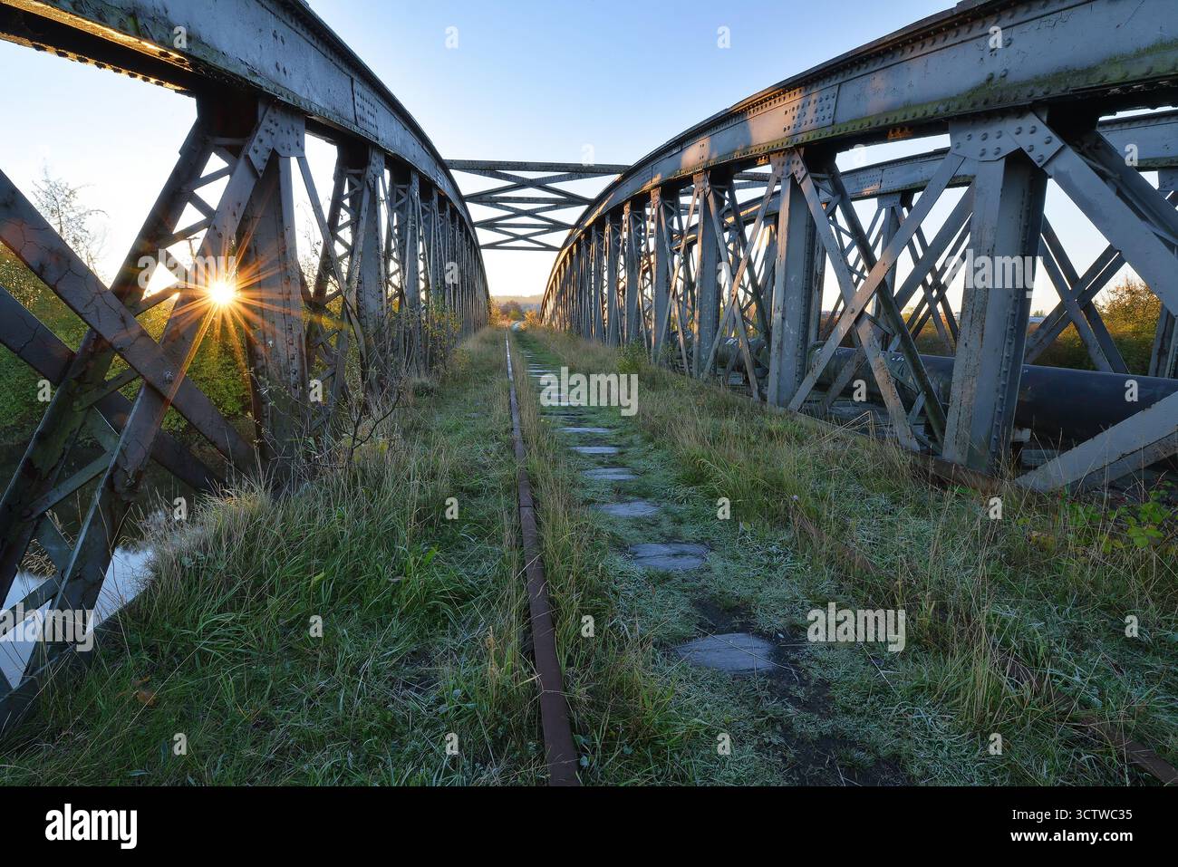 Verfallene Eisenbahnbrücke bei Sonnenaufgang mit Sonnenaufgang durch Stahlträger Stockfoto
