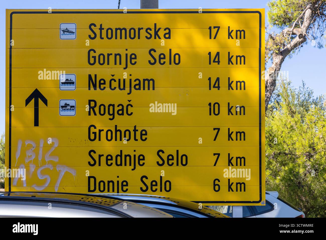 Ein hellgelbes Straßenschild gibt die Entfernungen zu mehreren kroatischen Inselstädten an, darunter Stomorska und Grohote. Die Szene deutet auf Reisen, Navigation, an hin Stockfoto