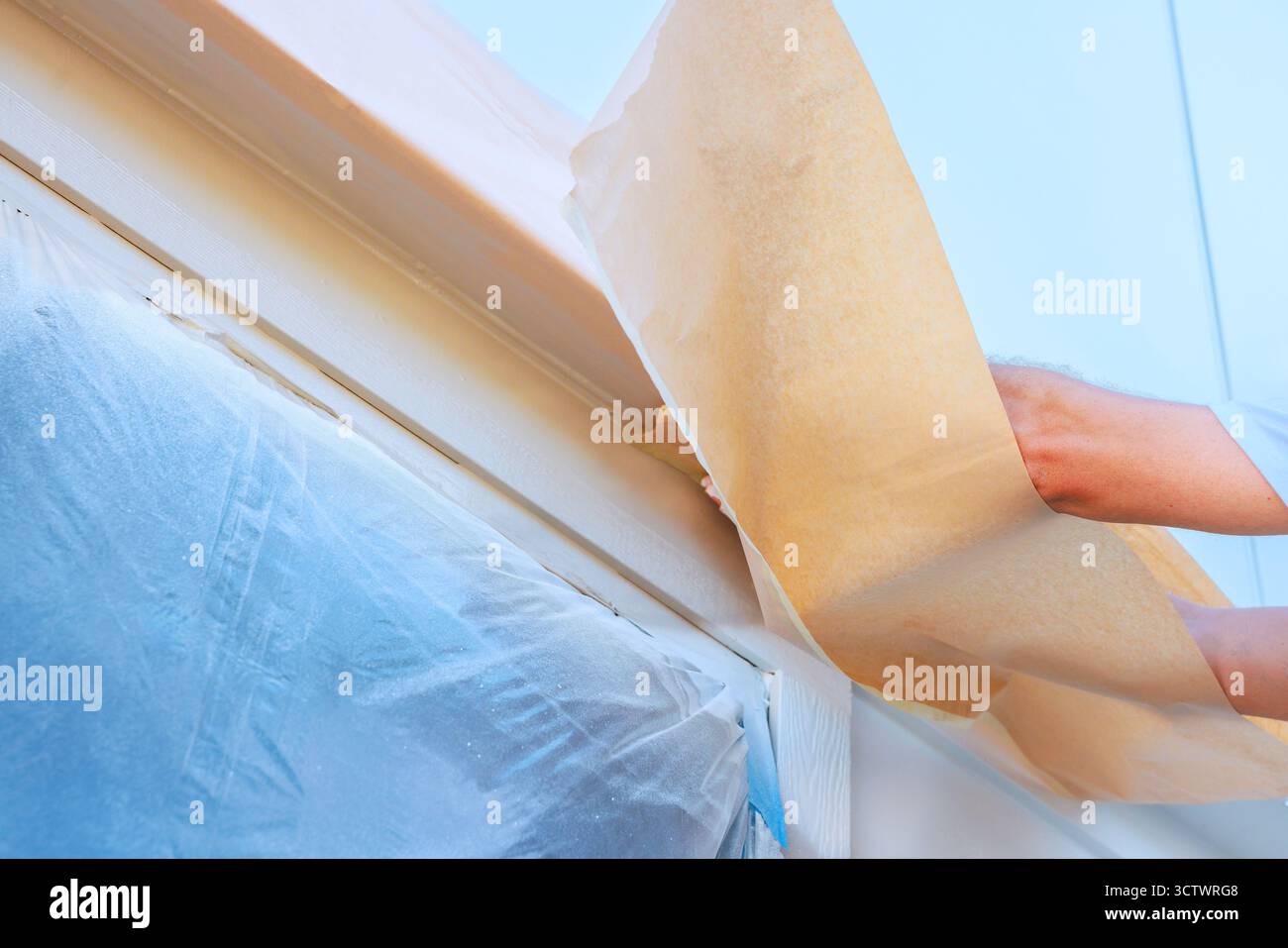 Der Maler löst das Abdeckband sanft von der Fensterverkleidung und legt frisch lackierte Oberflächen während der Renovierung frei. Stockfoto Der Maler löst das Abdeckband sanft von der Fensterverkleidung und legt frisch lackierte Oberflächen während der Renovierung frei. Stockfoto