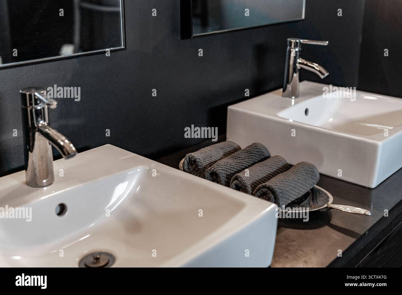 Nahaufnahme mit zwei weißen Waschbecken und grauen Handtüchern im modernen schwarzen Bad Stockfoto