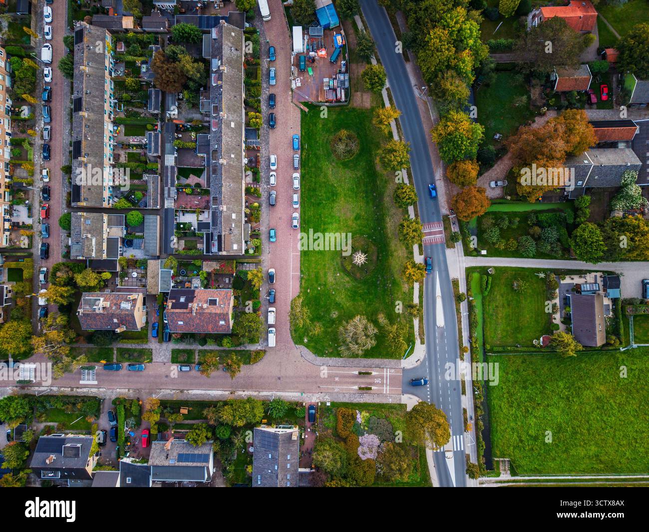 Aus der Vogelperspektive der Wohngegend Reihen von Häusern mit Gärten, zentralem grünen Park, gekrümmter Straße und offenen grasbewachsenen Feldern mit organisierter urb Stockfoto