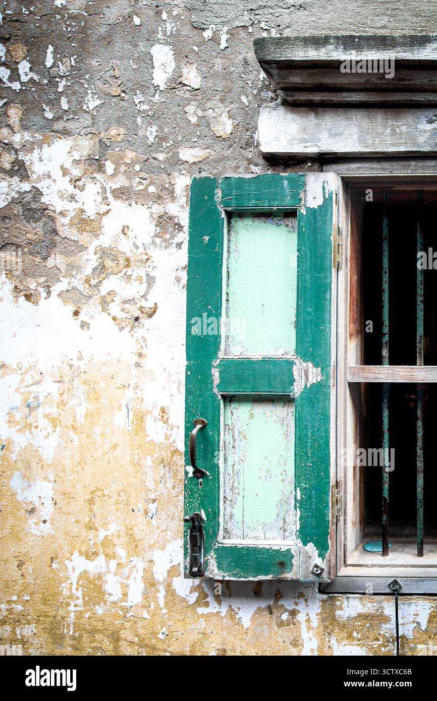 Vertikales Vintage-grünes Fenster mit abblätternder Farbe auf einer verwitterten, strukturierten Wand. Erfasst Art déco-Stil und Architekturgeschichte. Stockfoto
