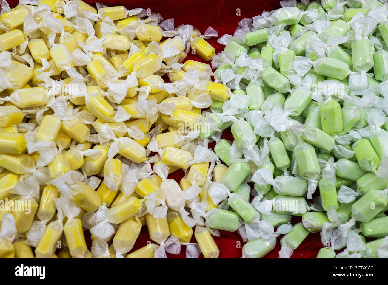 Nahaufnahme traditioneller thailändischer Toffee (durianische und pandanische Aromen) auf einer roten Oberfläche. Einzeln verpackt, beliebte thailändische Süßigkeiten. Stockfoto