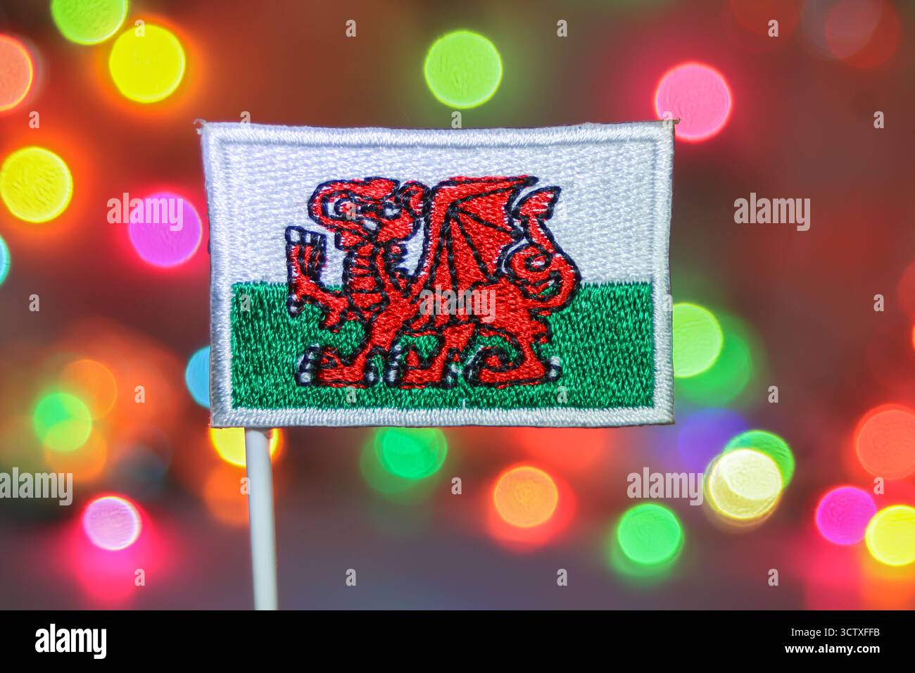 Nahaufnahme einer detailreich gestickten walisischen Flagge vor einem mehrfarbigen, weichen Bokeh, ideal für Weihnachten und Neujahr. Stockfoto