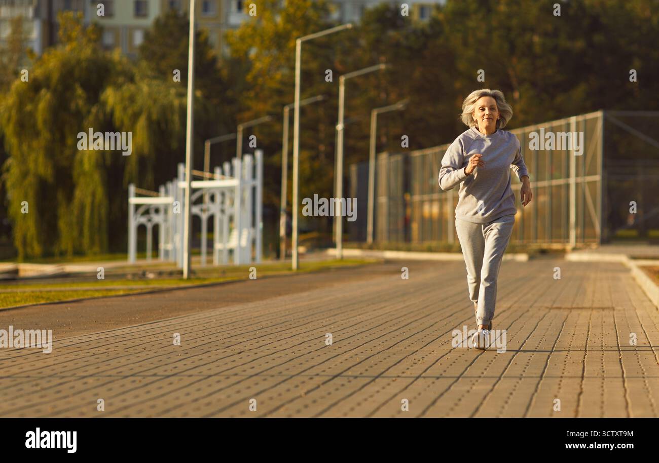 Aktive Seniorin joggt draußen im Park und trägt Sportswear am sonnigen Morgen Stockfoto