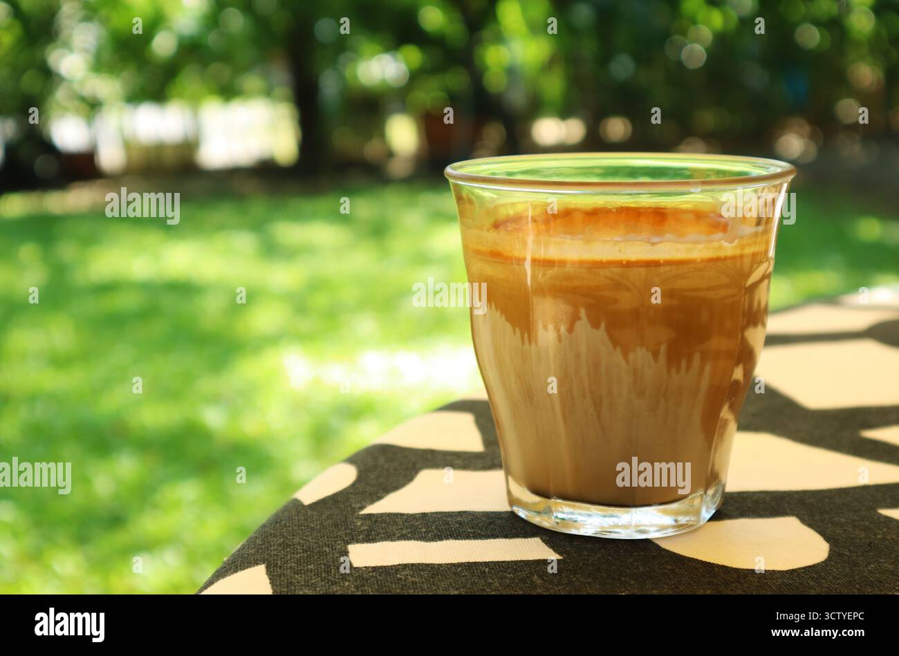 Ein Glas schmutzigen Latte-Kaffee wird auf dem Gartentisch serviert Stockfoto