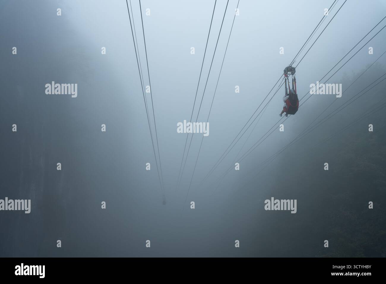 Seilbahn, die in dichtem Nebel über einem steilen Tal schwingt Stockfoto