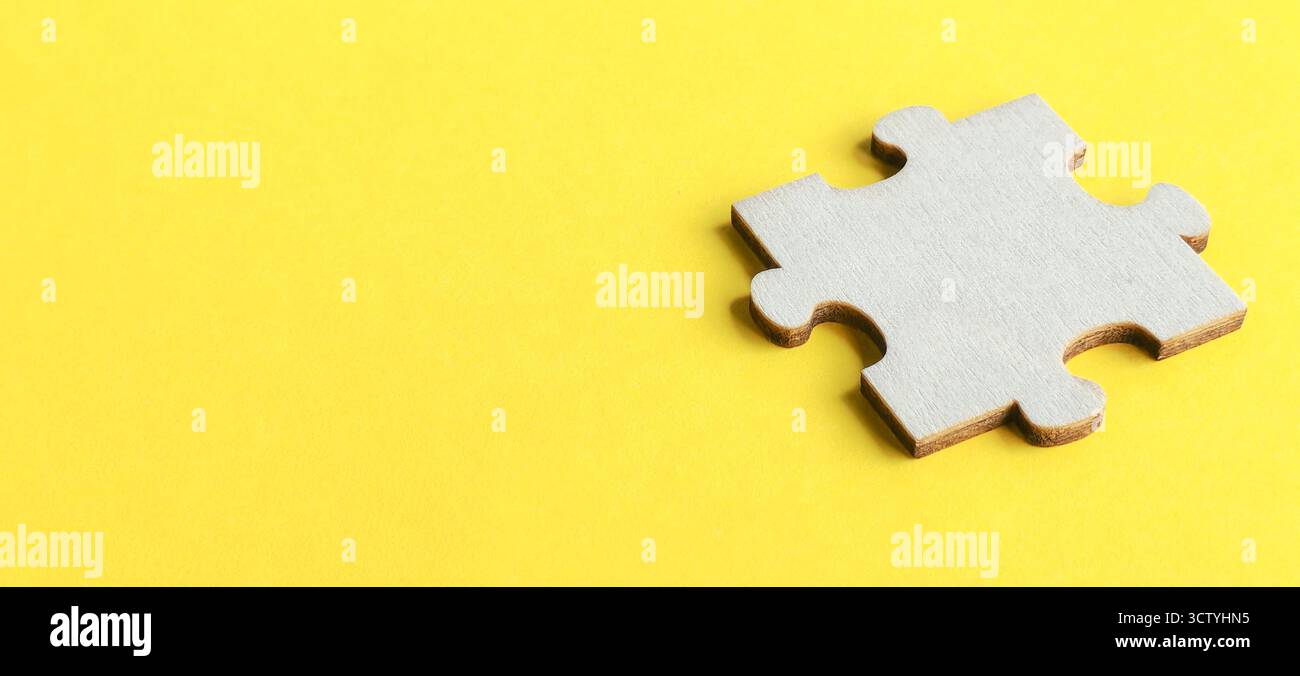 Einzelnes Puzzleteil aus Holz auf einem leuchtend gelben Hintergrund mit viel Kopierraum für Text- und Designelemente. Stockfoto