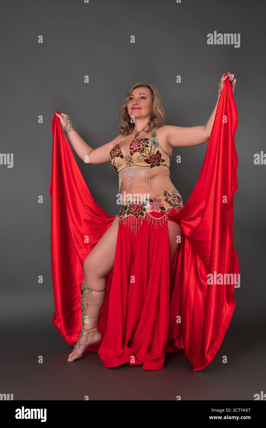 Verspielte Erwachsene Tänzerin mittleren Alters, die sich in Tanzkostüm kleidet - BH-Top, roter langer Rock mit Schlitz und sie trägt keine Schuhe, Performi Stockfoto