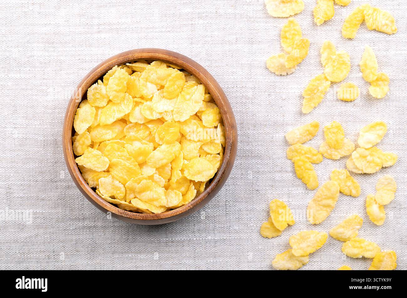 Cornflakes oder Cornflakes in einer Holzschale auf Leinen von oben. Frühstückszerealien aus toastenden Flocken von Mais oder Mais. Stockfoto