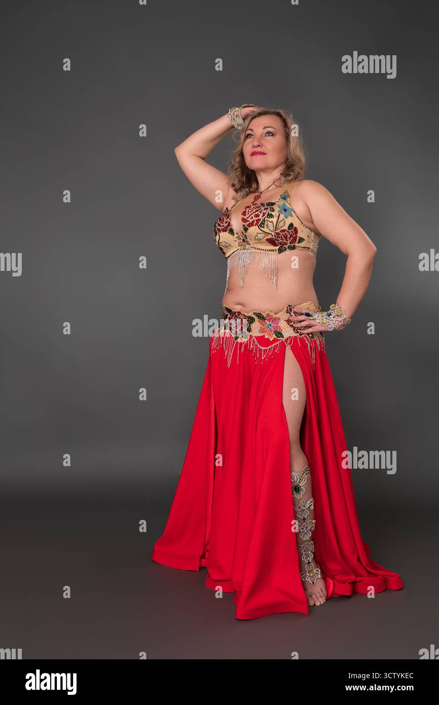 Inspirierendes Models und Bauchtänzerin mit Hand im Haar, gekleidet in Tanz-Outfit - Bralette und roter langer Rock mit Schlitz barfuß stehend Stockfoto